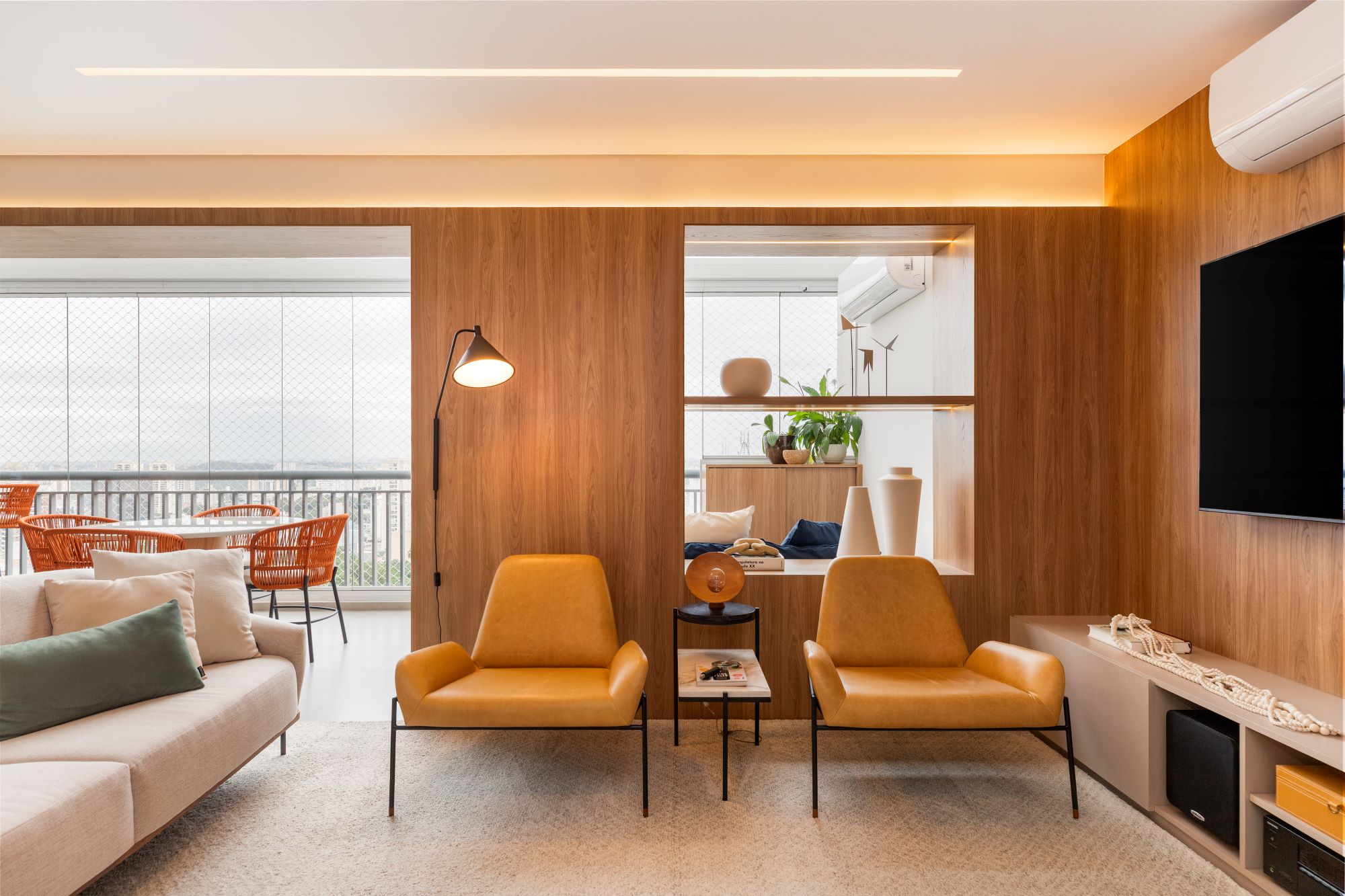 Sala de estar com painéis de madeira, duas poltronas de couro caramelo e vista para a varanda