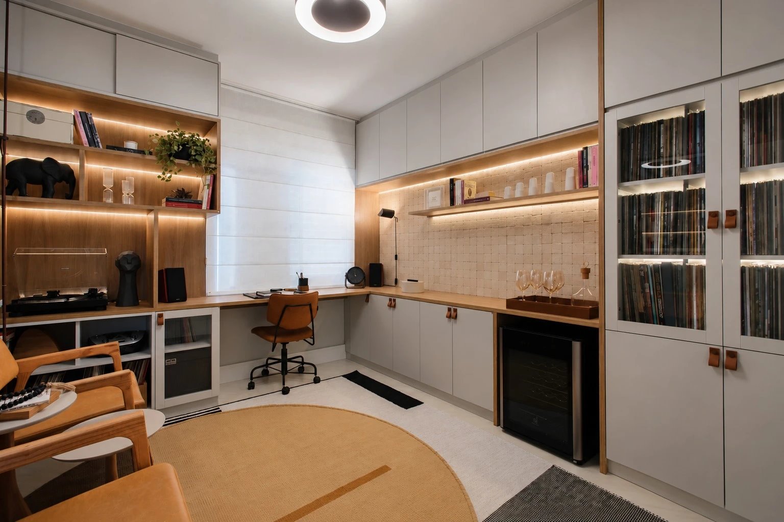 Projeto SE: home office com estantes iluminadas, toca-discos, bancada em L com cadeira caramelo e cristaleira de discos